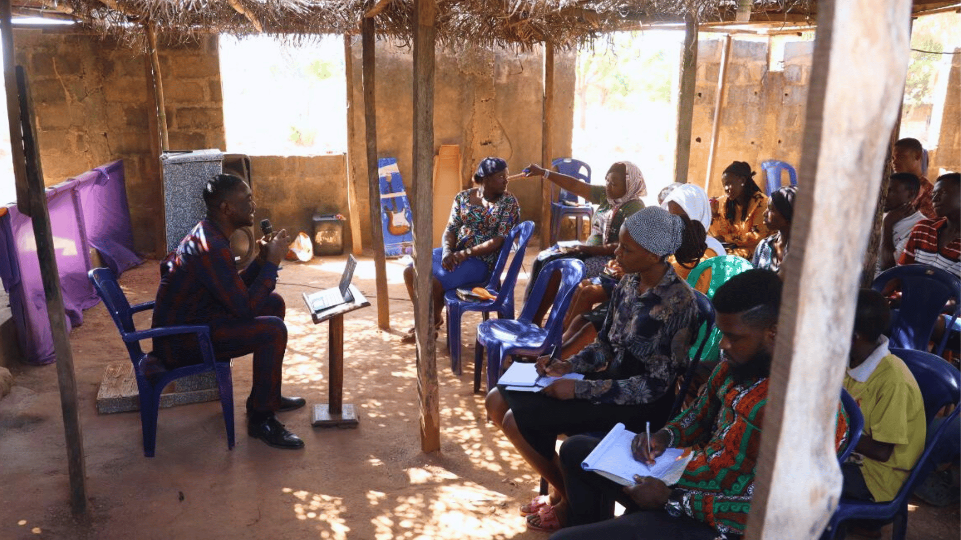A teacher speaking with a microphone as participants take notes during a small-group training session